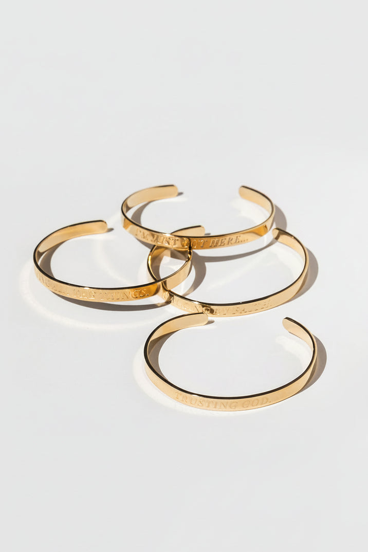 Flat lay of 4 gold bangles with shadowed lighting – engraved Christian affirmation bracelets for spiritual encouragement.