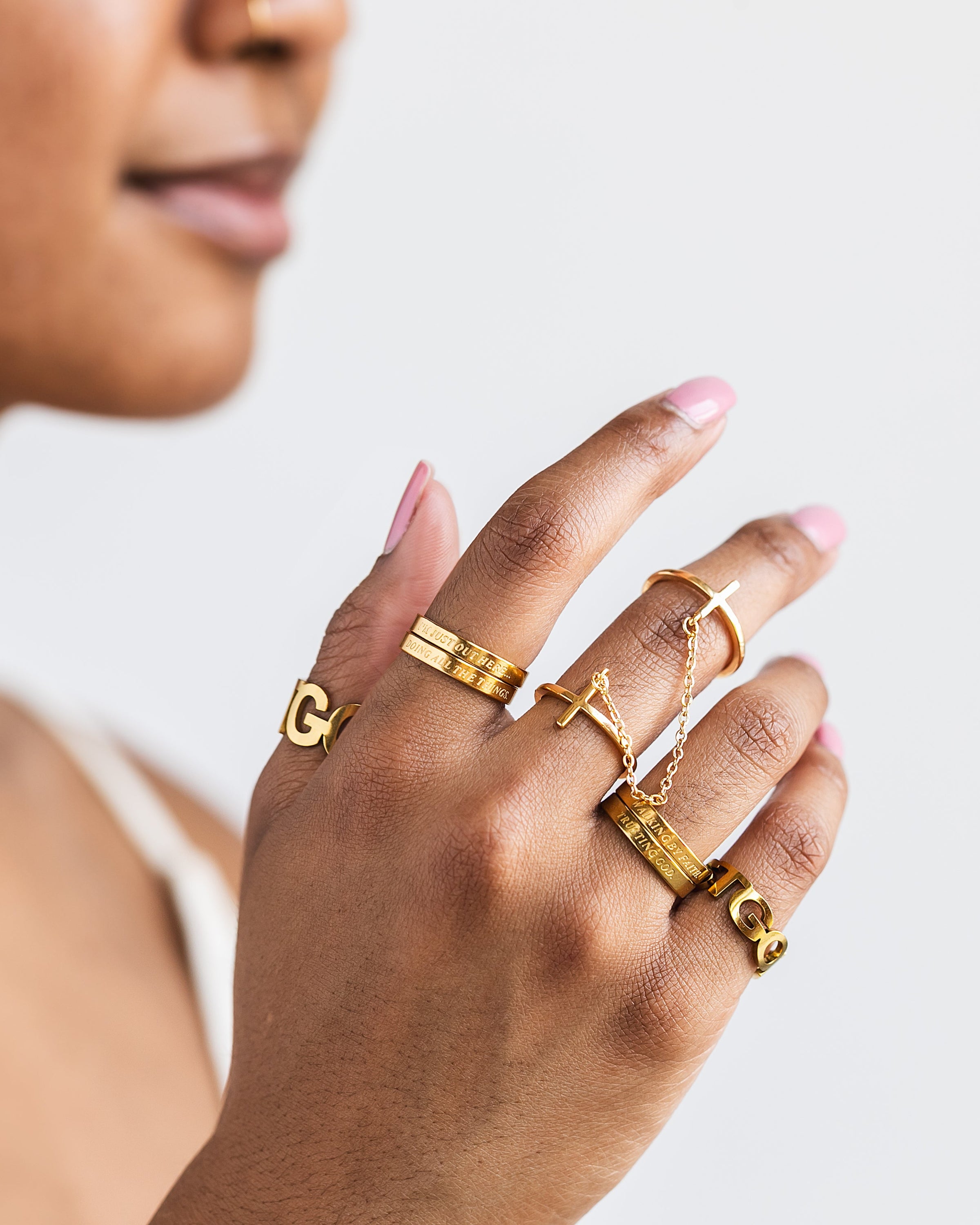 Close-up of woman’s hand wearing Christian statement rings in gold including cross rings, "Trust God" rings, and scripture-inspired faith jewelry — bold faith-based accessories for stylish women.