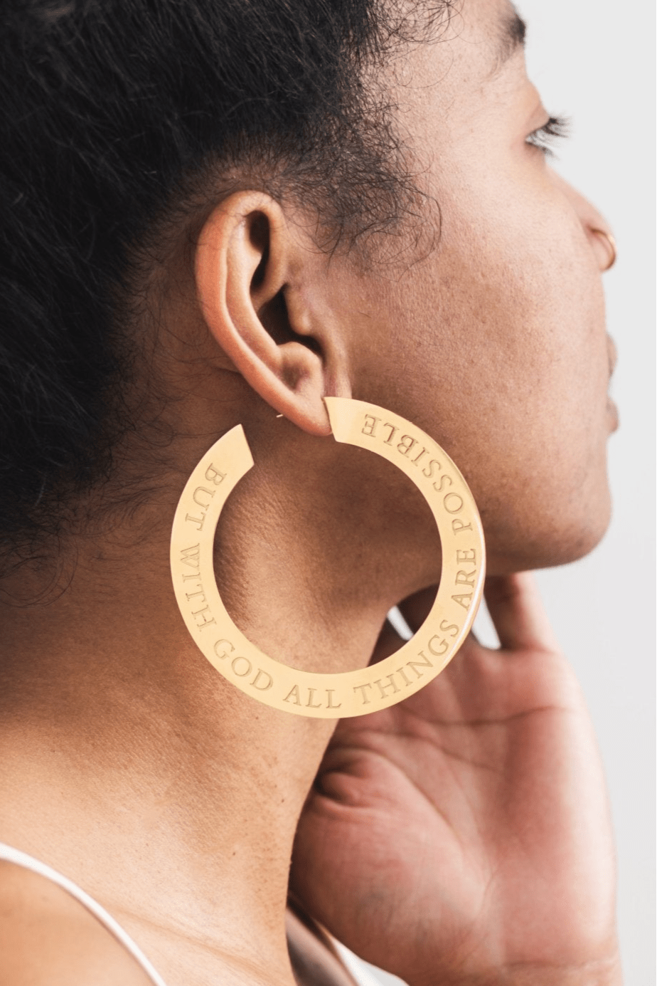 Close-up of woman wearing large 18k gold plated hoop earring engraved with “But With God All Things Are Possible” — bold Christian statement earrings by A Meaningful Mood for faith-filled fashion.