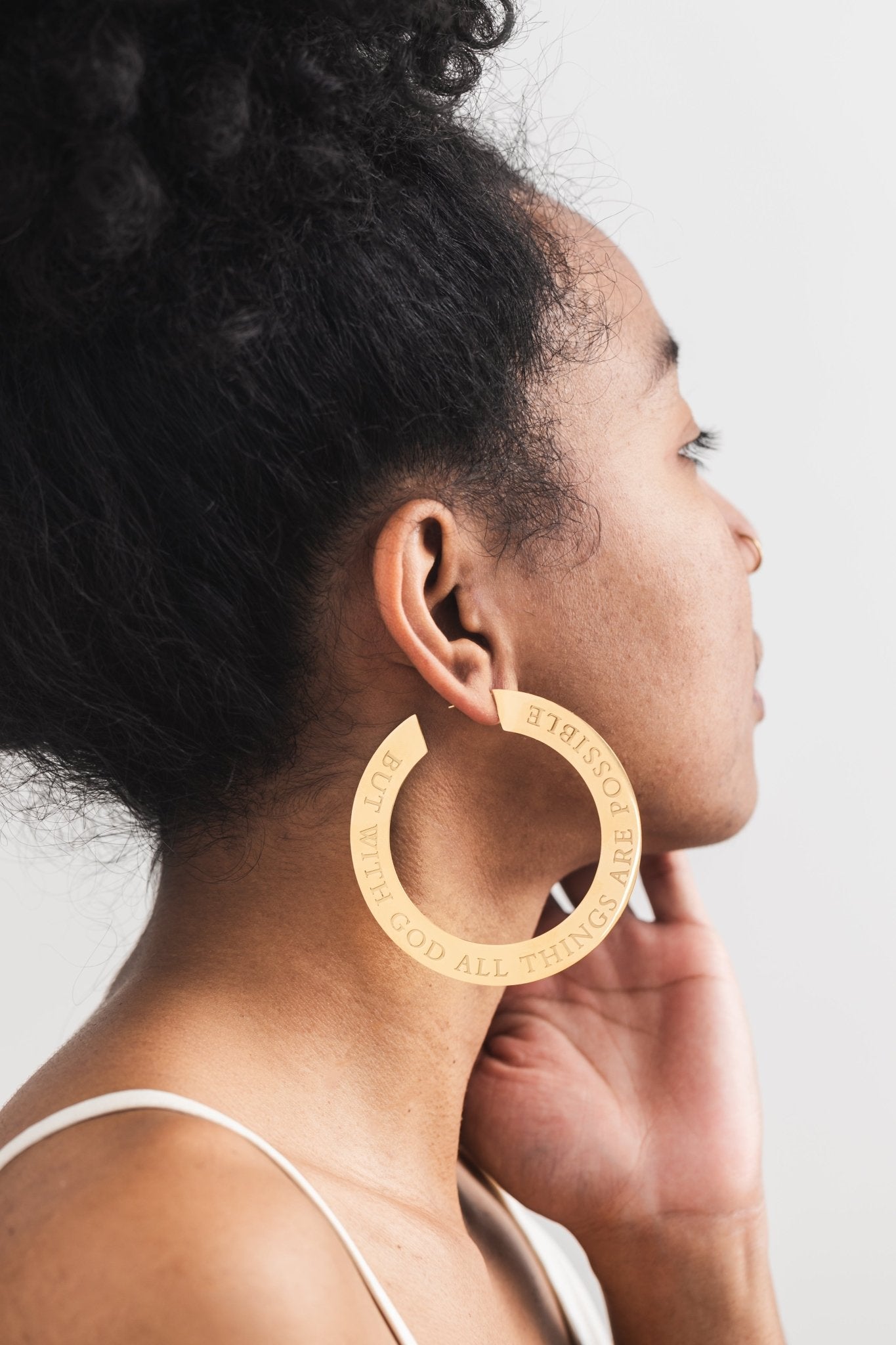 Side profile of woman wearing large 18k gold plated hoop earring engraved with “But With God All Things Are Possible” — bold Christian statement earrings by A Meaningful Mood for faith-filled fashion.