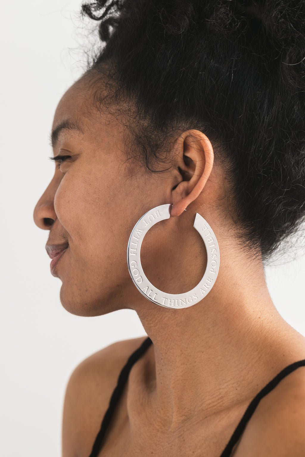 Close-up of woman wearing large stainless steel Christian hoop earrings engraved with “But with God all things are possible” — bold scripture-inspired jewelry by A Meaningful Mood designed to reflect your faith with style.