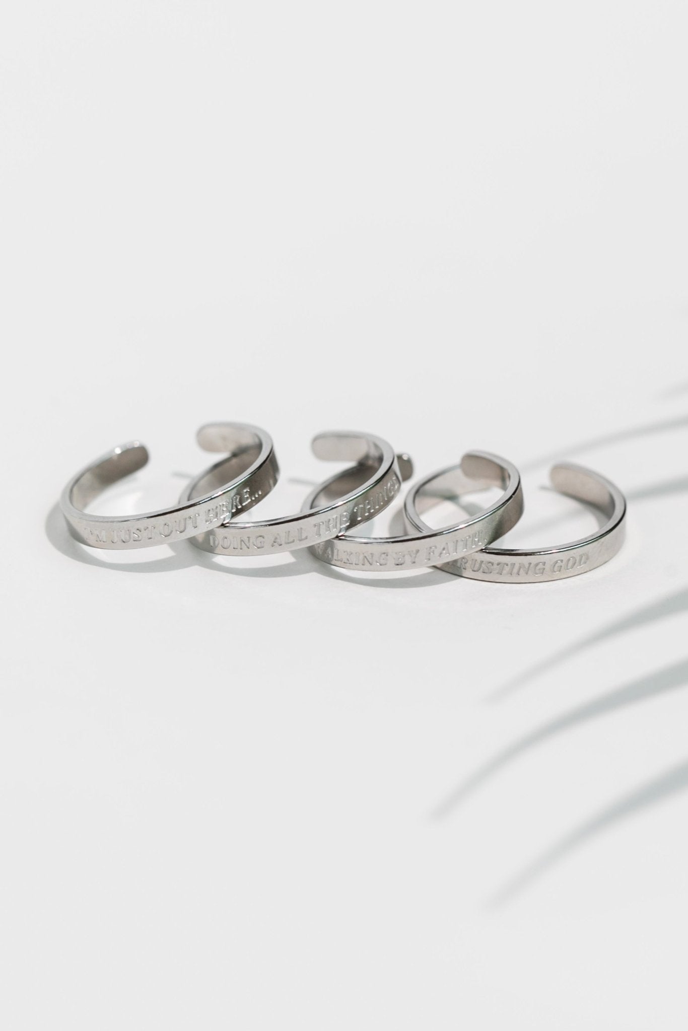 Four silver stainless steel engraved rings laid flat in soft lighting, each inscribed with faith-inspired phrases from the Faith Reflections Ring Set by A Meaningful Mood.