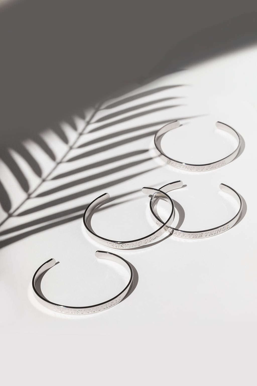 Flat lay of four stainless steel bangles with shadowed lighting – engraved Christian affirmation bracelets for spiritual encouragement.