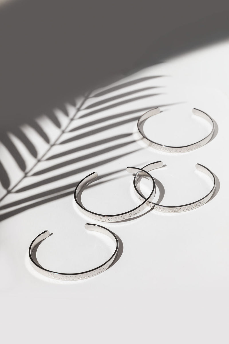 Flat lay of four stainless steel bangles with shadowed lighting – engraved Christian affirmation bracelets for spiritual encouragement.