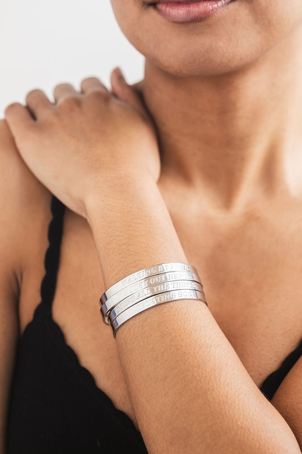 Woman wearing four stacked engraved stainless steel bangles on her wrist – stylish and meaningful Christian faith jewelry for everyday wear.