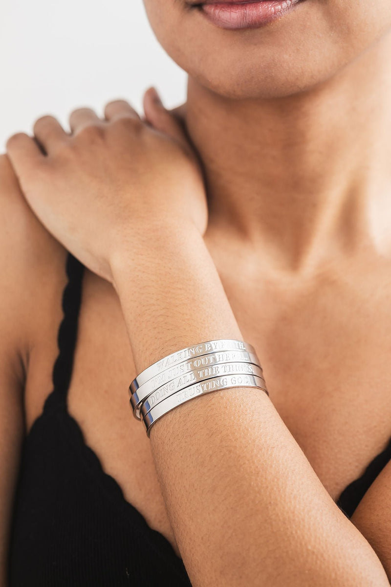 Woman wearing four stacked engraved stainless steel bangles on her wrist – stylish and meaningful Christian faith jewelry for everyday wear.