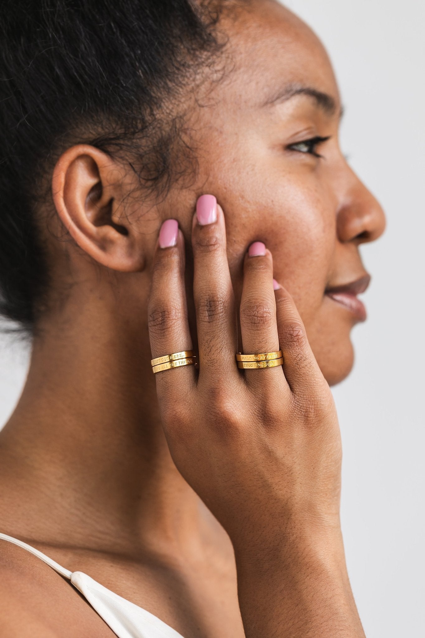 Side profile of a woman smiling with both hands near her face, wearing stacked gold faith-based rings from the Faith Reflections Ring Set by A Meaningful Mood.