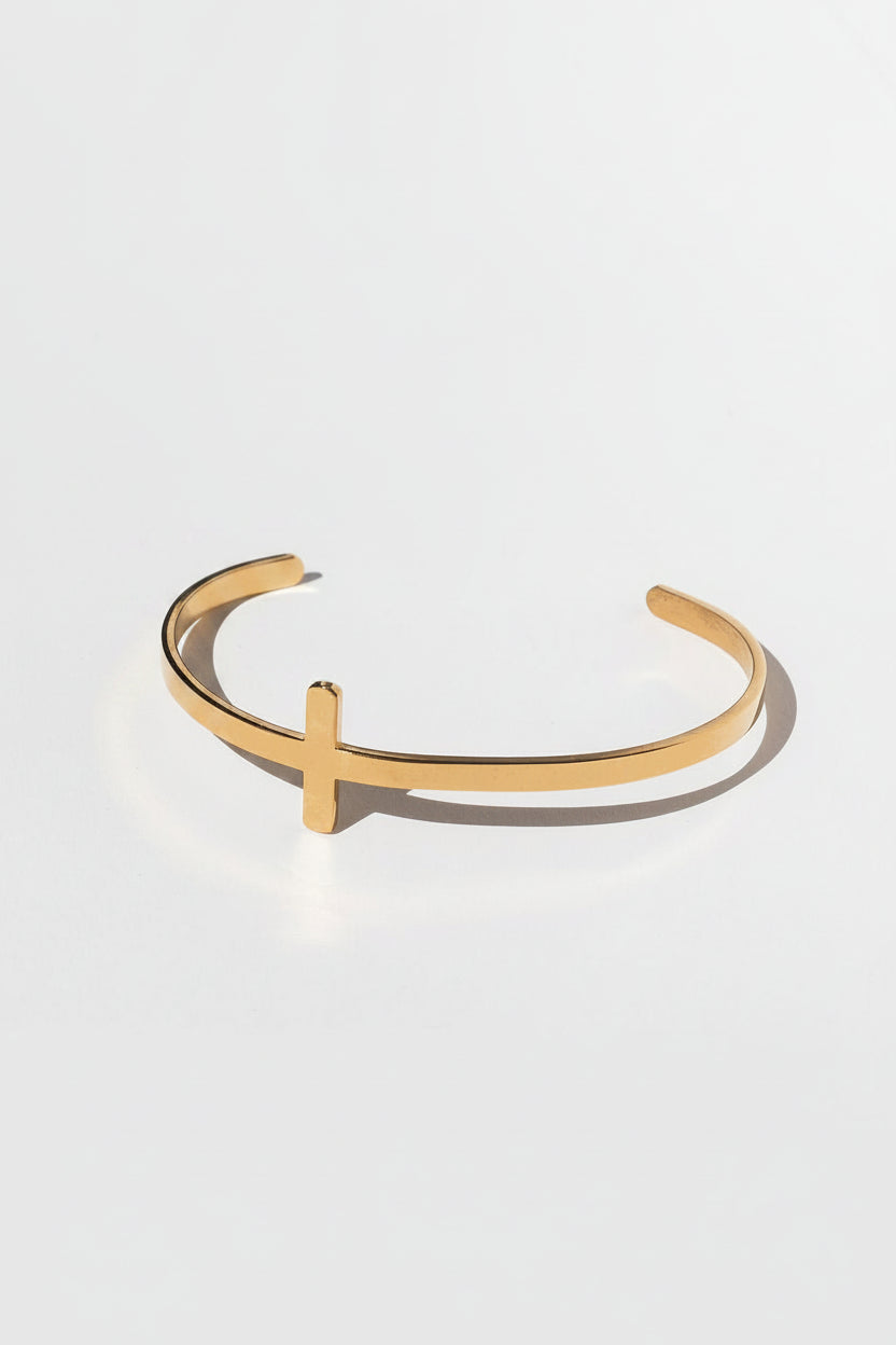 Minimalist 18k gold plated bangle featuring a bold cross detail, photographed against a white backdrop with leaf shadows.