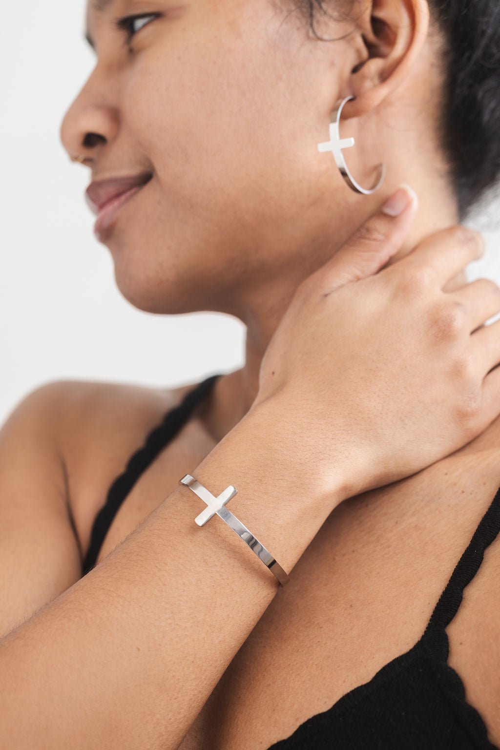 Faith-based jewelry set with stainless steel cross bangle and matching cross hoop earrings, worn by woman with natural style.