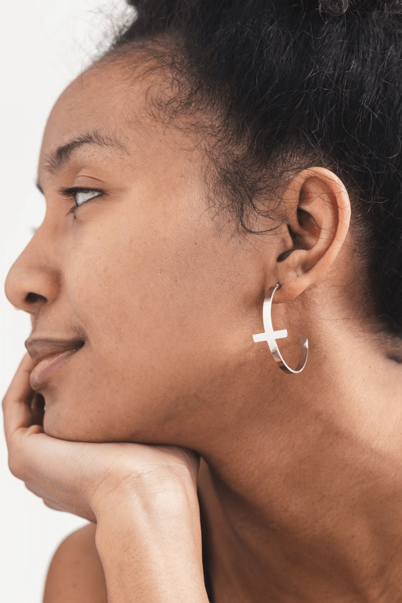 Close-up of a woman wearing a silver hoop cross earring on a white background