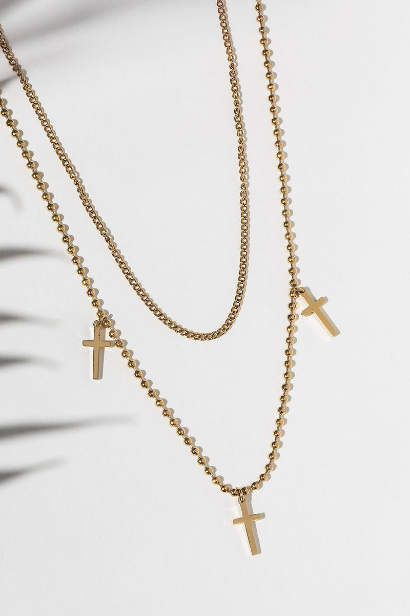 Flat lay of So Chic Cross Layered Necklace featuring 3 gold cross pendants on tiered chains