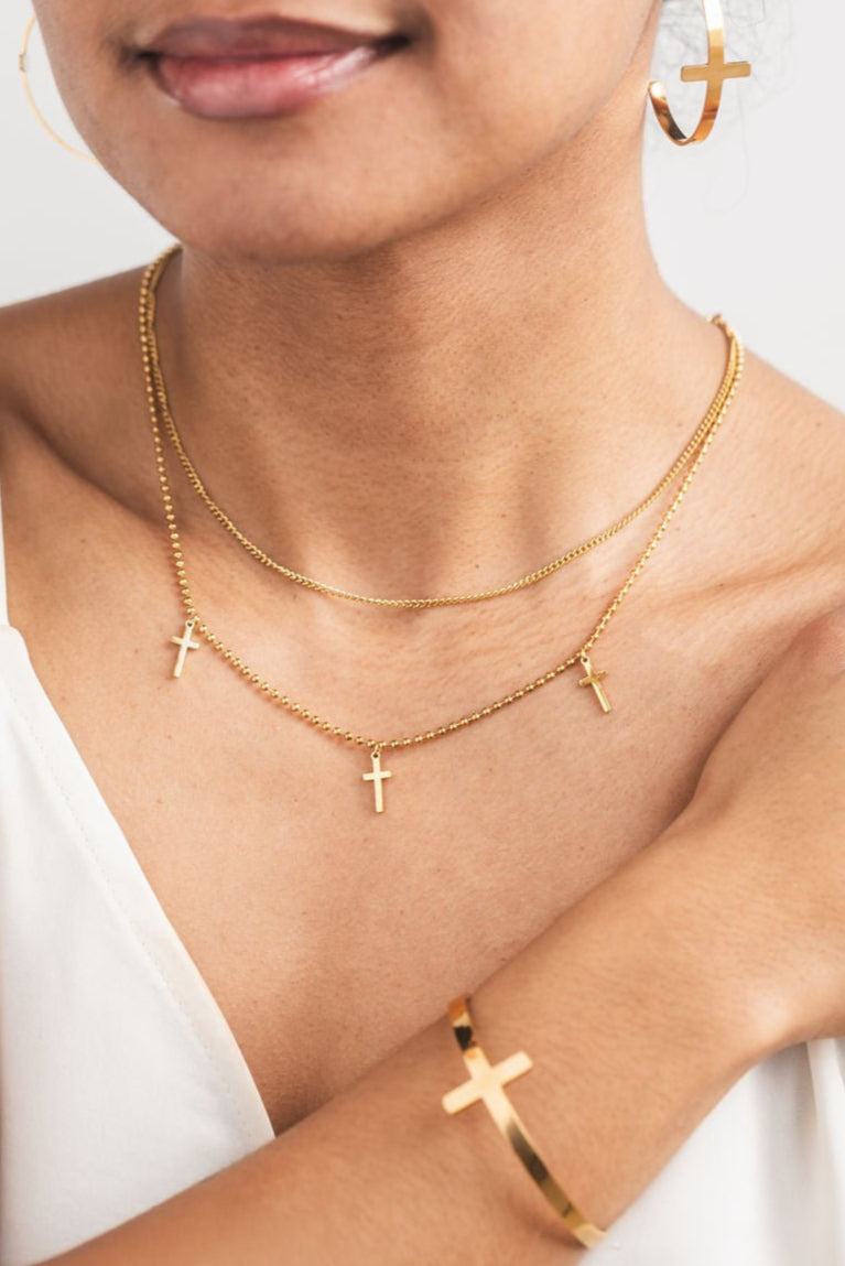 Model styled in full So Chic gold cross look with layered necklace, hoop earrings, and cross bangle