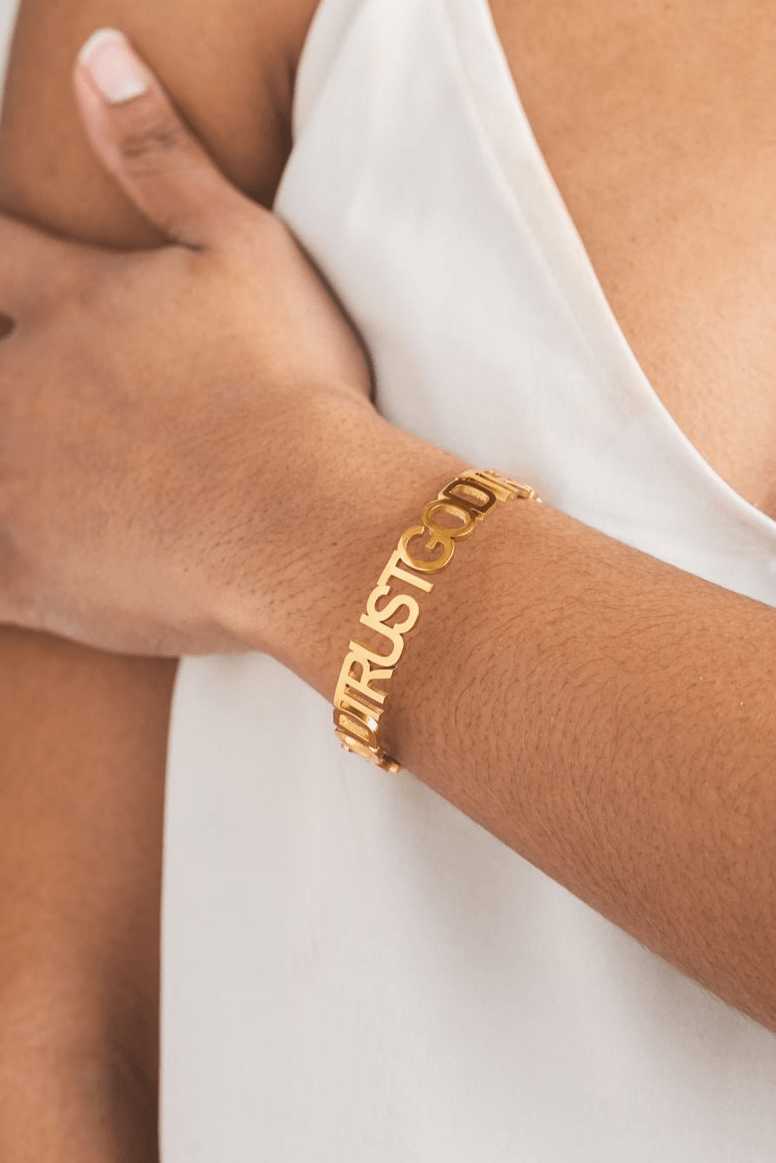 Close-up of a woman wearing the Trust God Bold Bangle in 18k gold plating from A Meaningful Mood — Christian jewelry designed to reflect faith in style with a powerful “TRUST GOD” cutout design.
