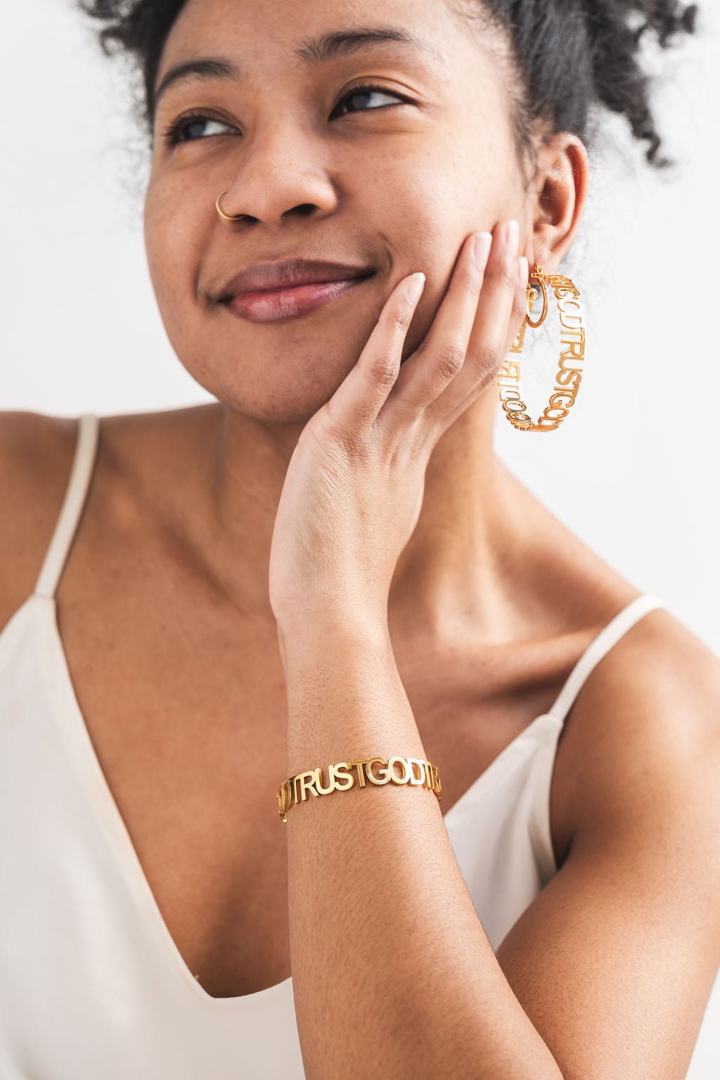 Smiling woman wearing 18k gold plated Trust God Bold Bangle and matching Trust God statement hoop earrings from A Meaningful Mood — faith-based jewelry that boldly reflects Christian values through fashion-forward design.