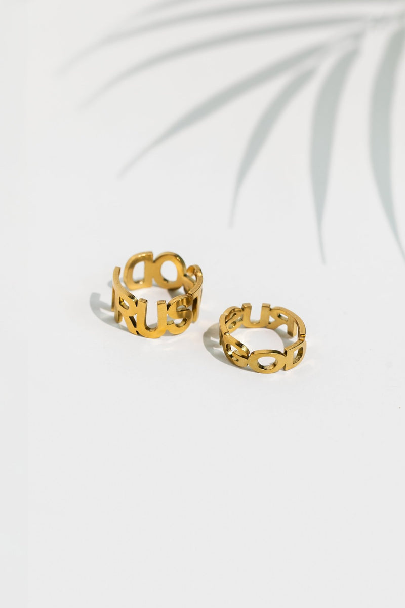Two Trust God rings in 18k gold-plated finish displayed side-by-side on a white surface with soft shadows, showcasing front and back views.