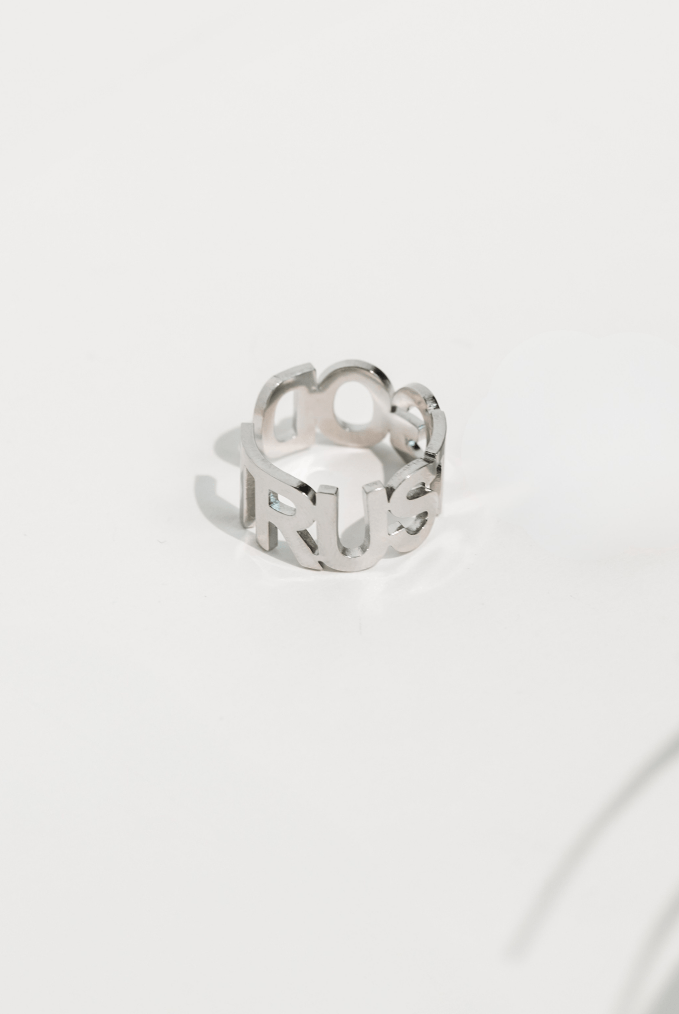 Shiny stainless steel cutout ring with the bold phrase “TRUST GOD” displayed in modern block lettering, photographed on a clean white background.