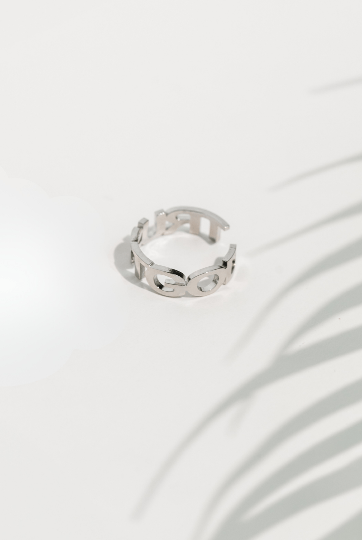 Side view of the stainless steel Trust God Ring showcasing the back cutout design and reflective finish, casting a soft shadow on a minimal white surface.