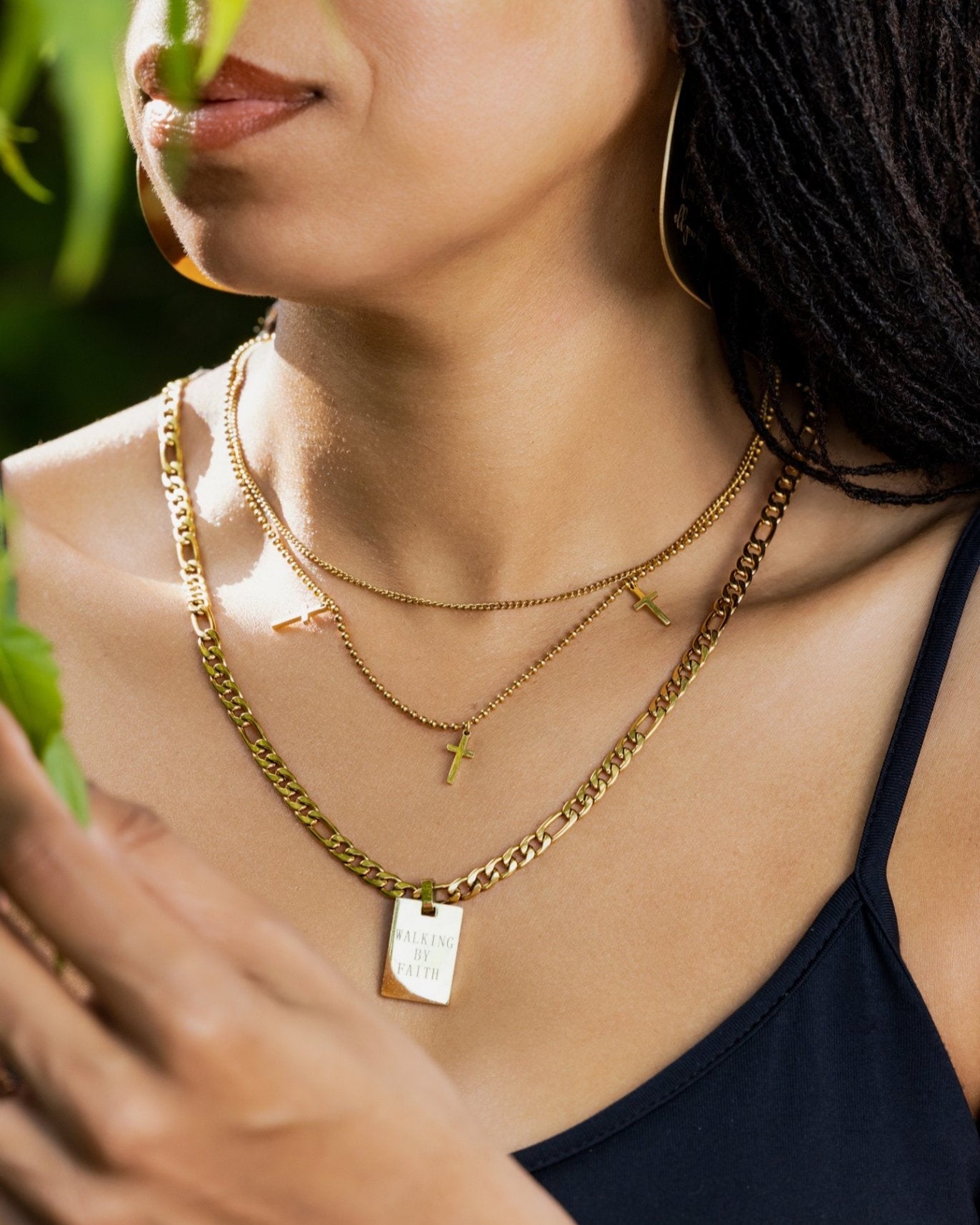 Woman wearing layered gold Christian necklaces including a "Walking by Faith" engraved pendant and small gold cross charms — inspirational Christian jewelry for women of faith.