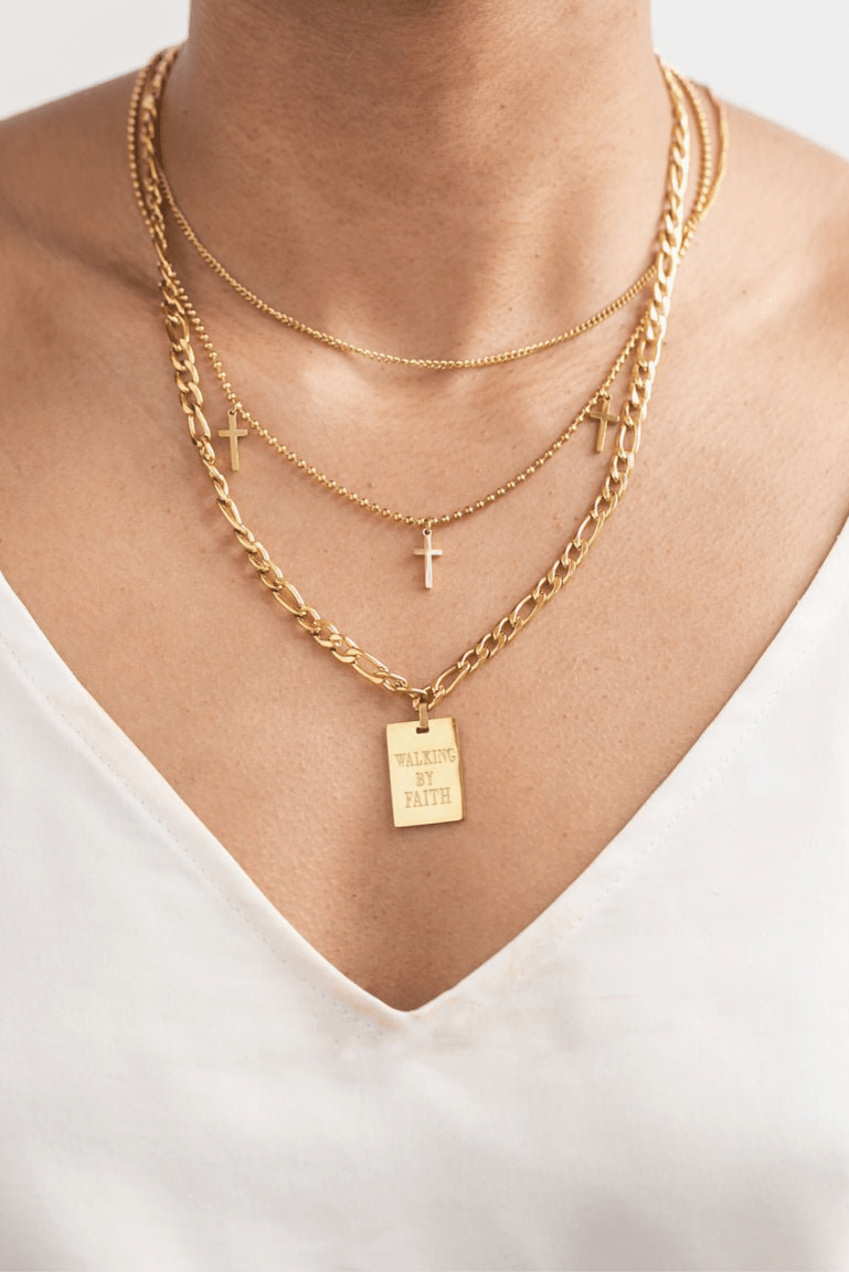 Model wearing a layered Christian necklace look, featuring the Walking By Faith Pendant Necklace paired with two-layered delicate gold cross necklace, styled over a white V-neck top for a faithful and fashionable statement.