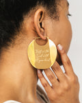 Gold earring with engraved text worn by a person
