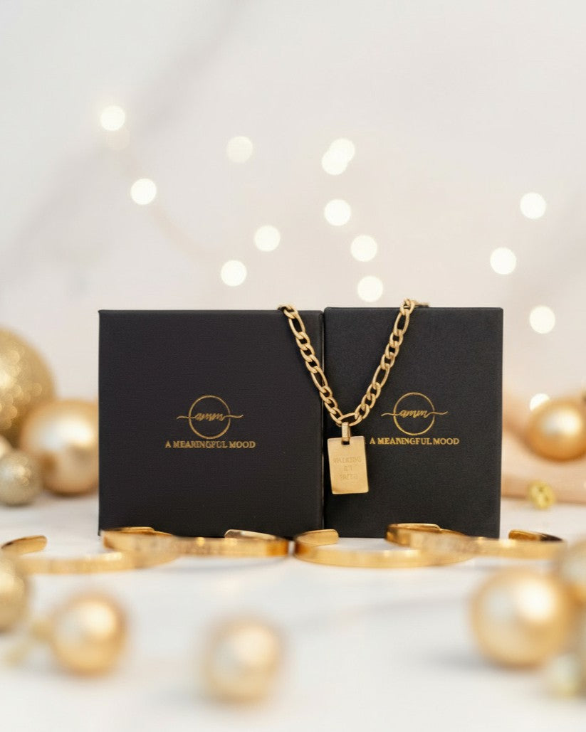 Gold necklace with a tag on a black box with 'A Meaningful Mood' branding, surrounded by gold ornaments.