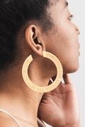 Close-up of woman wearing large 18k gold plated hoop earring engraved with “But With God All Things Are Possible”