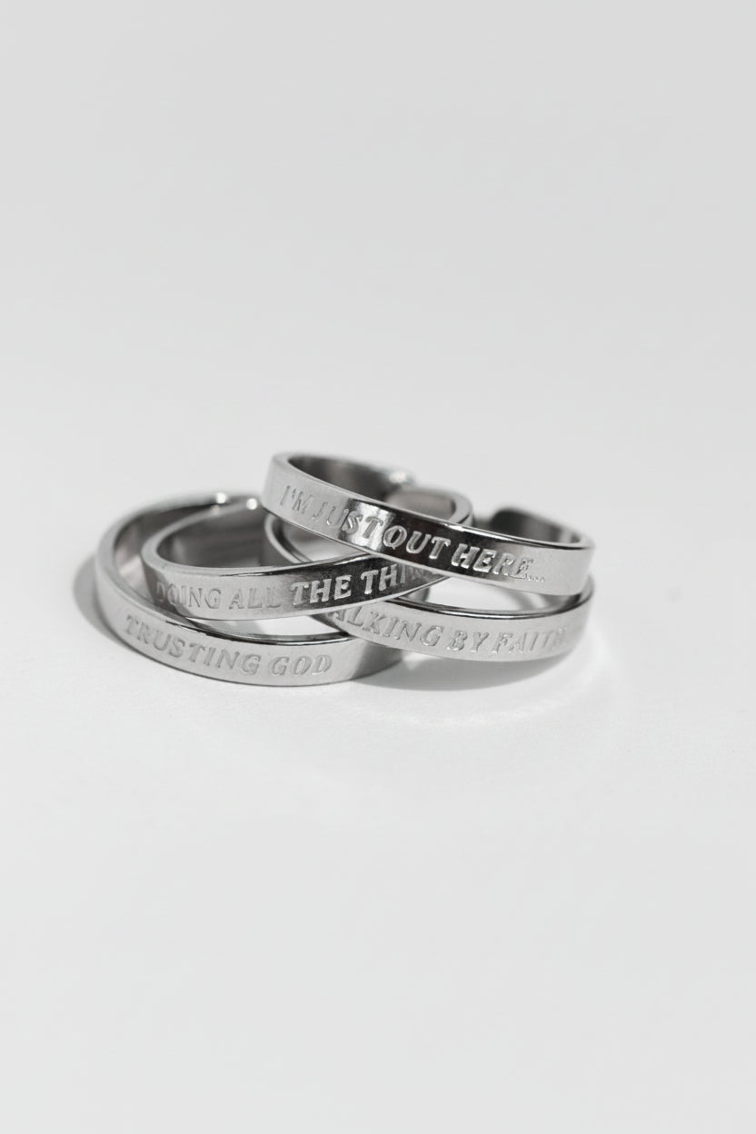 Stack of silver stainless steel rings engraved with “I’m Just Out Here…,” “Doing All the Things,” “Walking by Faith,” and “Trusting God,” part of the Faith Reflections Ring Set from A Meaningful Mood.