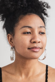 Close-up of woman wearing silver stainless steel "Trust God" hoop earrings from A Meaningful Mood. Christian statement earrings styled with natural makeup and gold nose ring. Faith-based jewelry for women who reflect their faith and style.